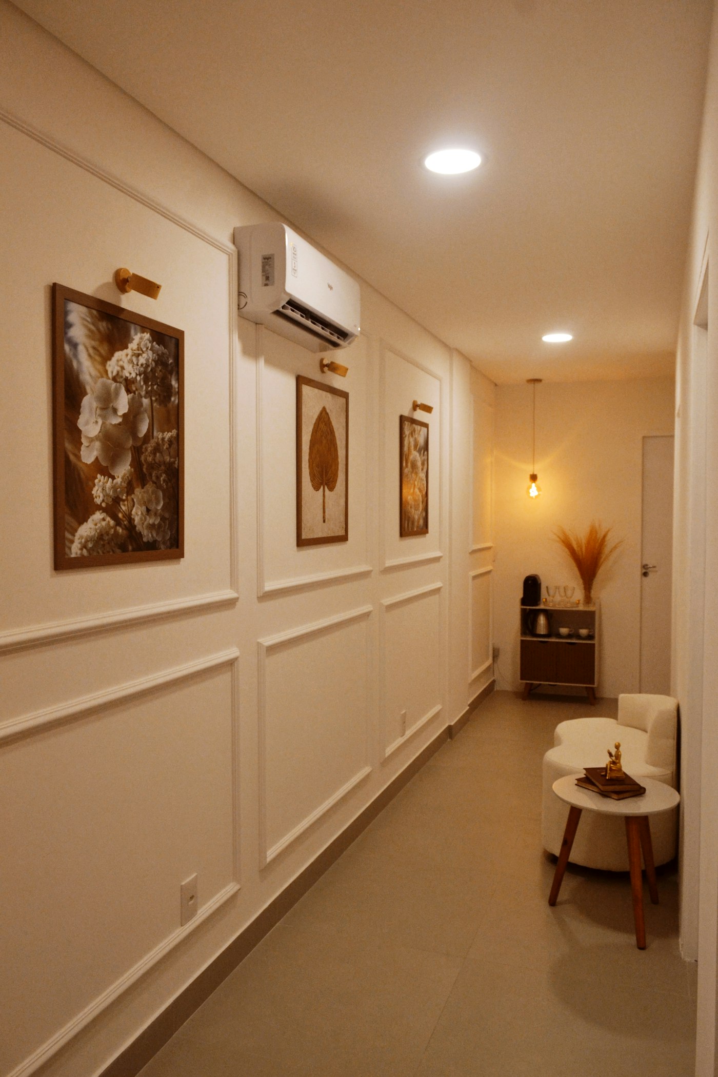 Quiet corridor with framed artwork, warm lighting and a small seating nook