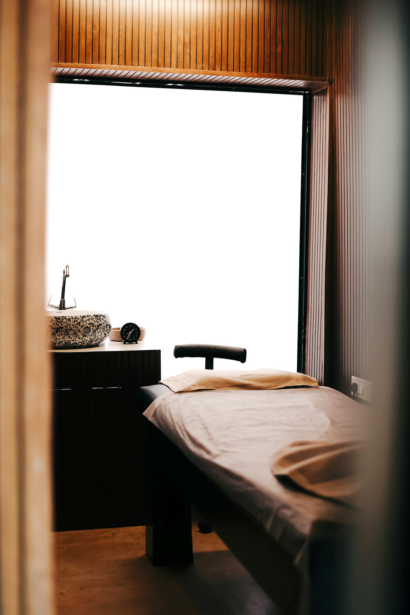 Treatment room with a padded treatment bed beside a tall, bright window
