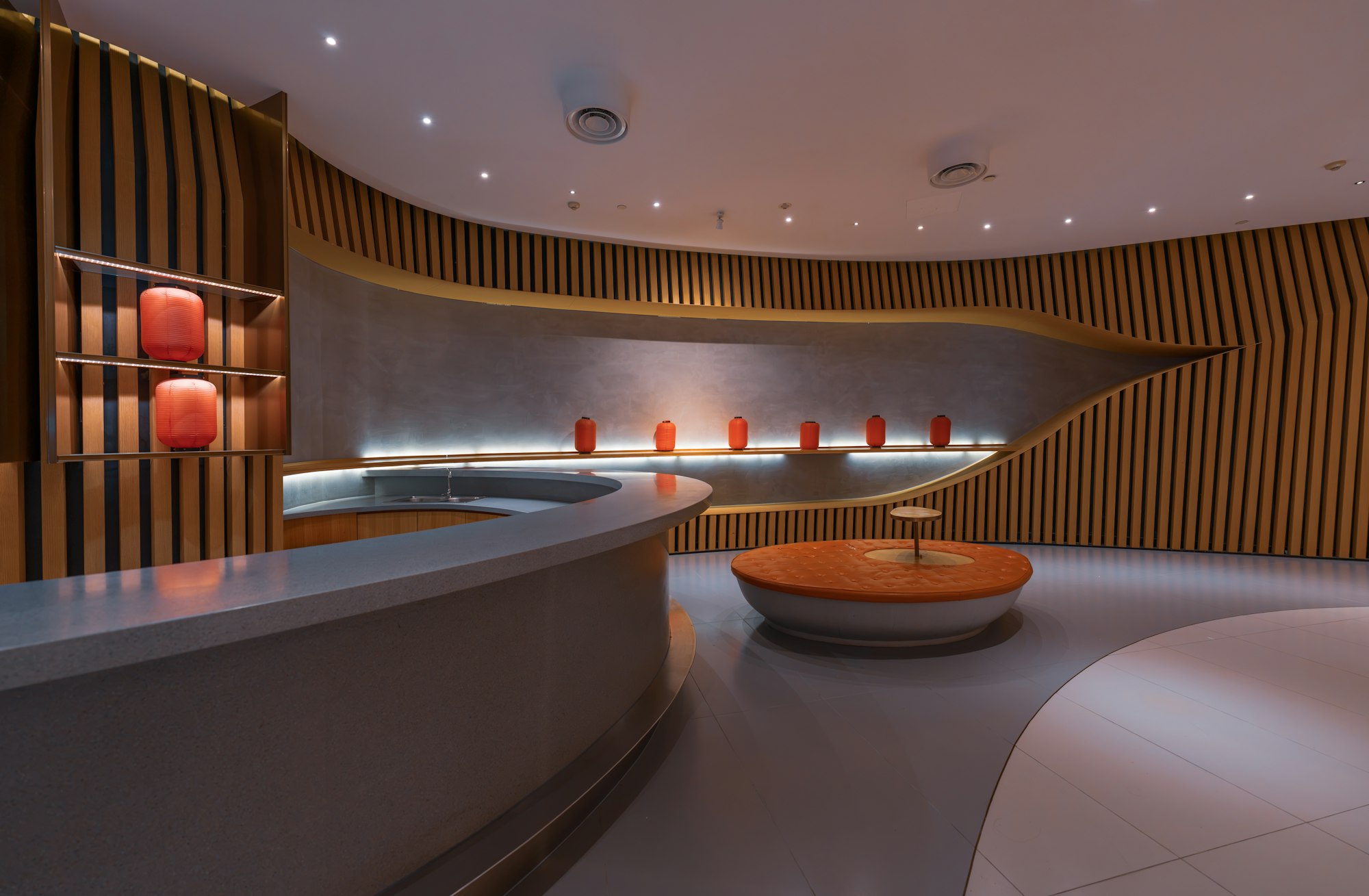 Office lounge and reception — curved reception counter and wood-slat walls with glowing red lamps in a softly lit lounge