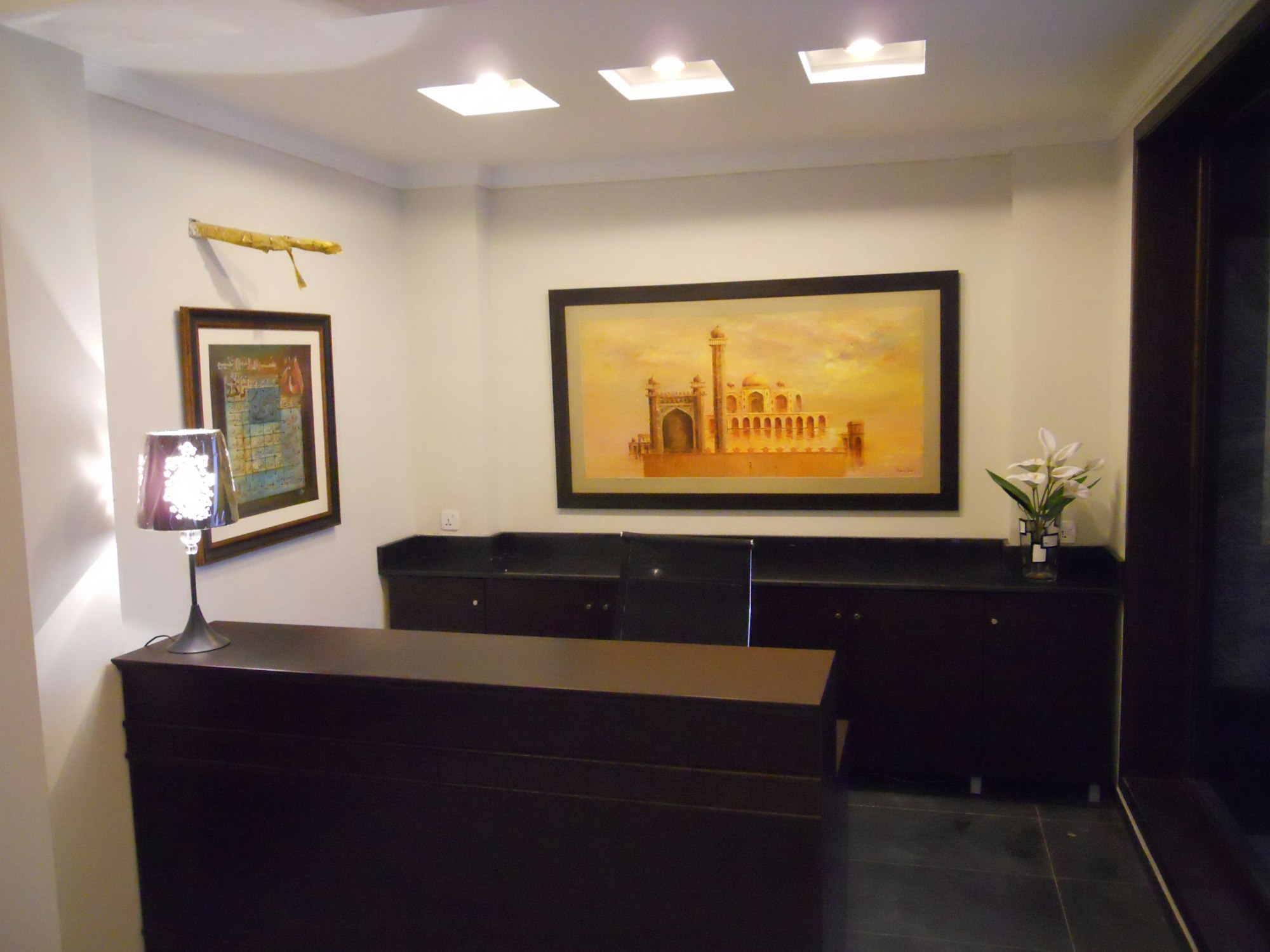 Reception area with a dark wood desk, framed landscape painting and warm ceiling lights