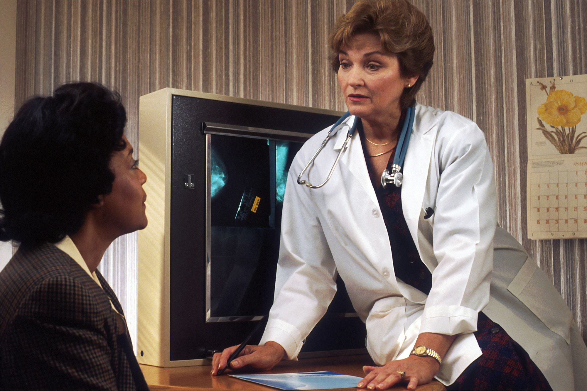 Provider in a white coat talking with a woman across a desk in a warmly lit office